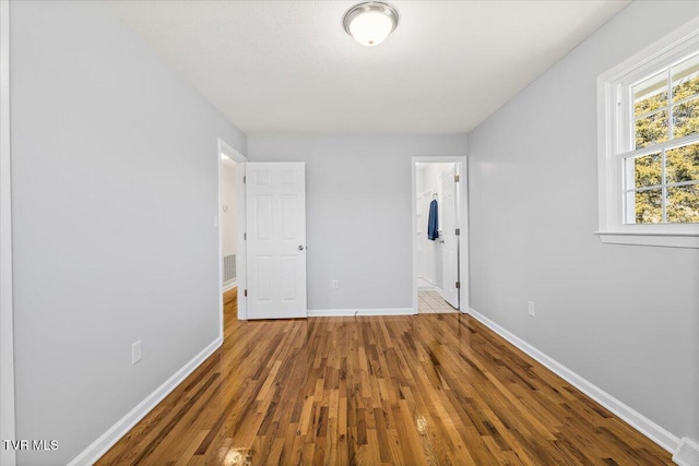 unfurnished bedroom featuring visible vents, connected bathroom, baseboards, and wood finished floors