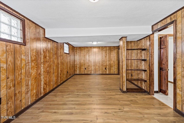 basement featuring light wood finished floors, baseboards, a textured ceiling, and wood walls