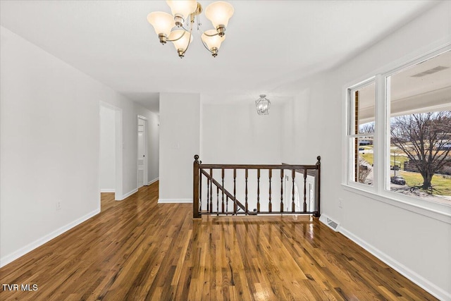 unfurnished room with dark wood-style floors, baseboards, visible vents, and a chandelier