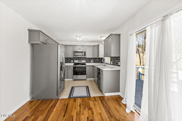 kitchen with stainless steel appliances, gray cabinets, light countertops, backsplash, and a sink