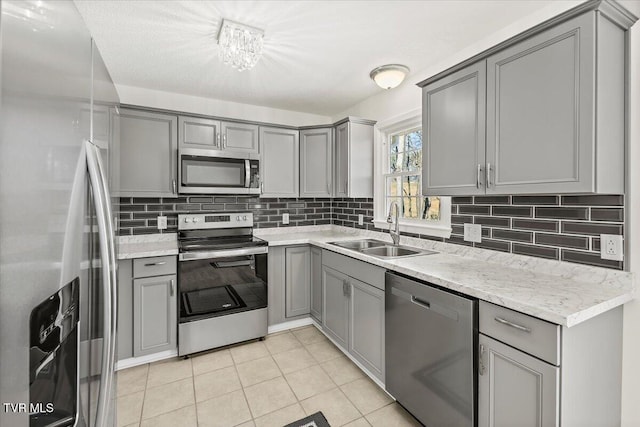 kitchen with light tile patterned floors, stainless steel appliances, tasteful backsplash, gray cabinets, and a sink