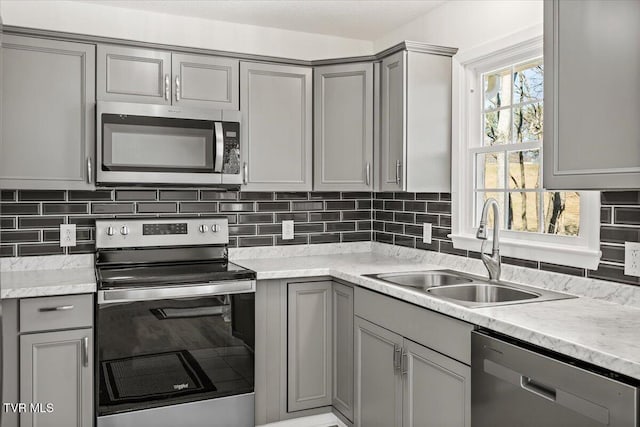 kitchen featuring tasteful backsplash, appliances with stainless steel finishes, a sink, and gray cabinetry