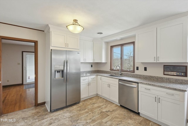kitchen featuring appliances with stainless steel finishes, white cabinetry, light stone counters, and a sink