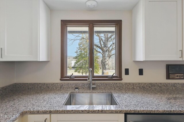 kitchen with stainless steel dishwasher, light stone countertops, a sink, and white cabinetry
