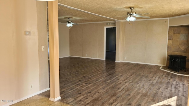 unfurnished living room with visible vents, a ceiling fan, ornamental molding, wood finished floors, and a wood stove