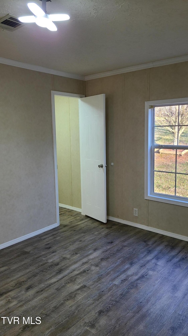 spare room featuring baseboards, wood finished floors, visible vents, and crown molding