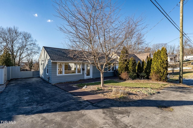 view of front facade with a shingled roof, driveway, and fence