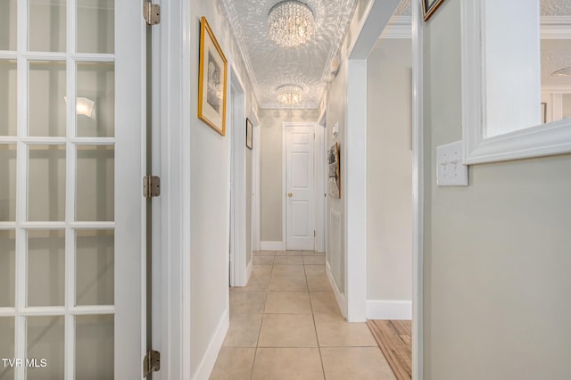 hallway with a textured ceiling, light tile patterned flooring, baseboards, an inviting chandelier, and crown molding