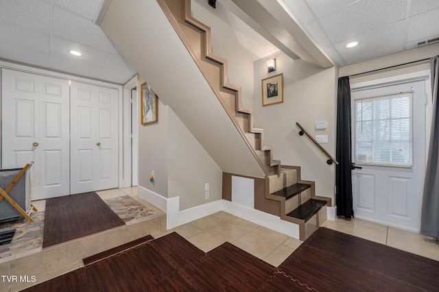 foyer entrance with light tile patterned floors, a drop ceiling, stairs, and baseboards