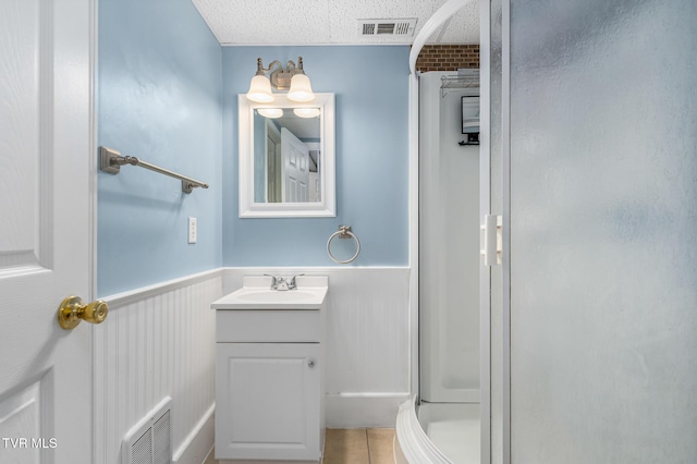 full bathroom with a wainscoted wall, vanity, visible vents, and a stall shower