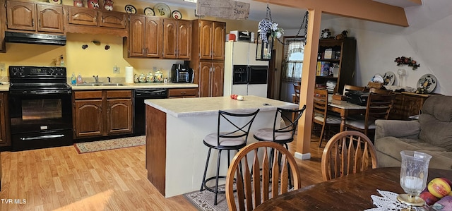 kitchen with under cabinet range hood, light countertops, light wood-type flooring, black appliances, and a sink