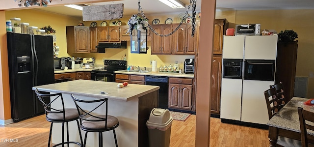 kitchen featuring a center island, a breakfast bar area, light countertops, under cabinet range hood, and black appliances