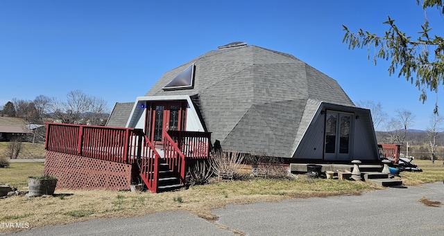 view of side of property with a wooden deck and roof with shingles