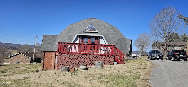 back of house with roof with shingles, a wooden deck, and a lawn