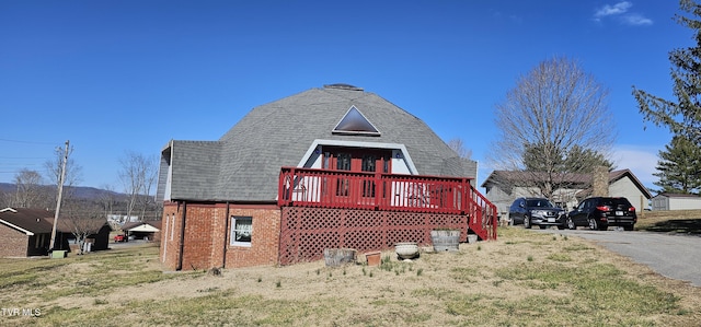 exterior space featuring brick siding, roof with shingles, a yard, and a wooden deck