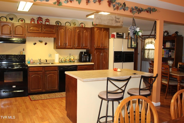 kitchen featuring light wood-style floors, under cabinet range hood, light countertops, black appliances, and a sink