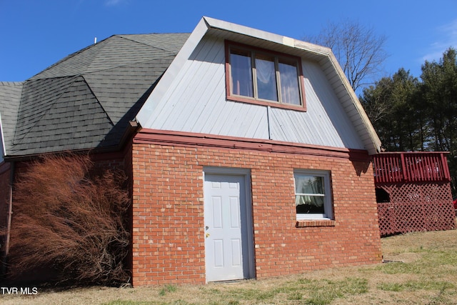 rear view of house with a shingled roof, brick siding, a lawn, and a wooden deck