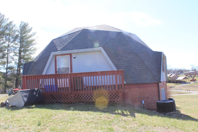 rear view of property with a deck, roof with shingles, and a lawn