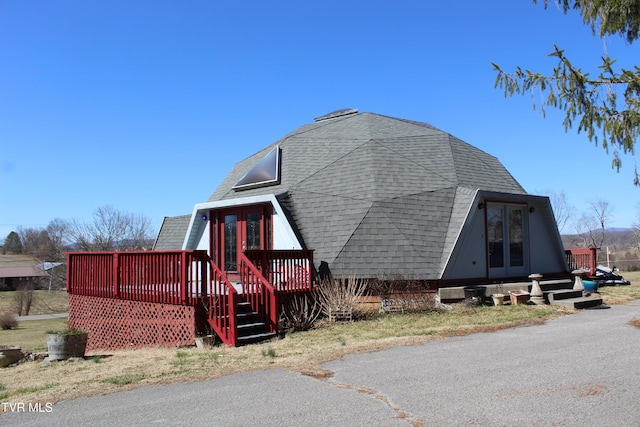 view of side of property with roof with shingles and a wooden deck