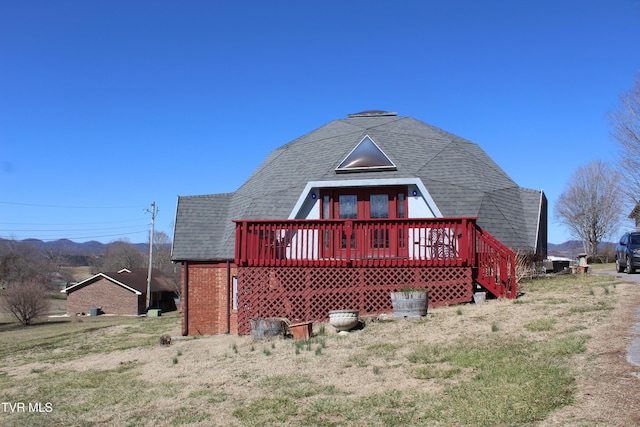 back of house featuring roof with shingles, brick siding, and a deck