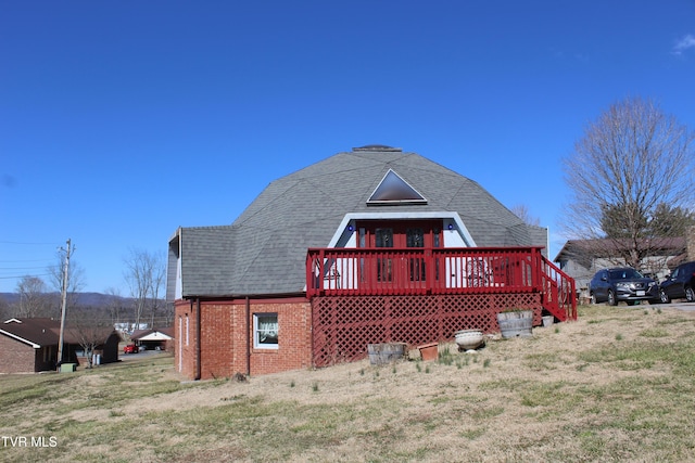 rear view of property featuring brick siding, a lawn, a deck, and roof with shingles