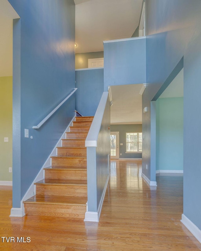 staircase with a high ceiling, wood finished floors, and baseboards