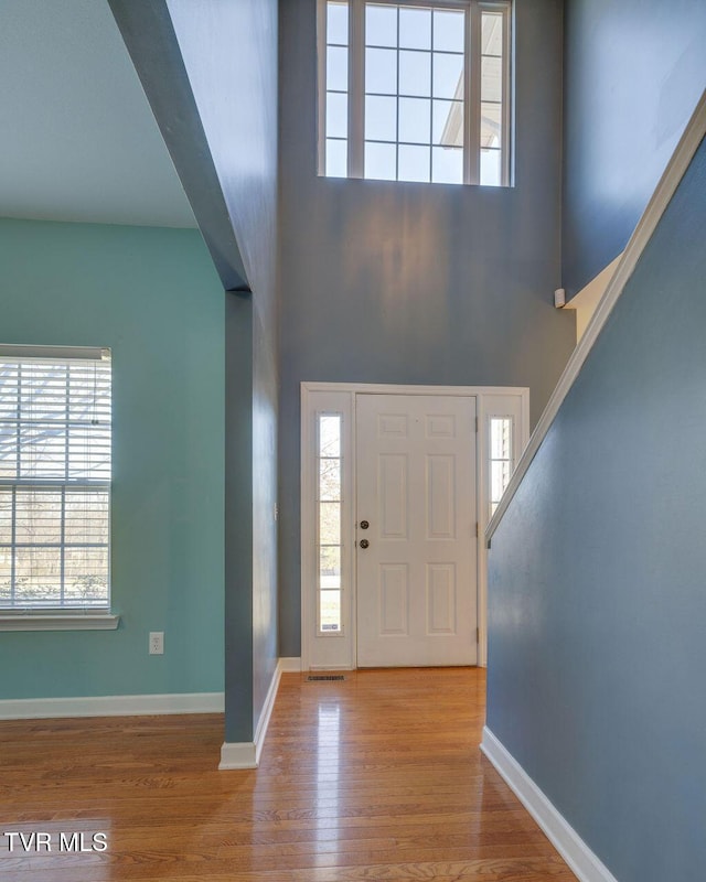 foyer entrance with a towering ceiling, light wood-style floors, and baseboards