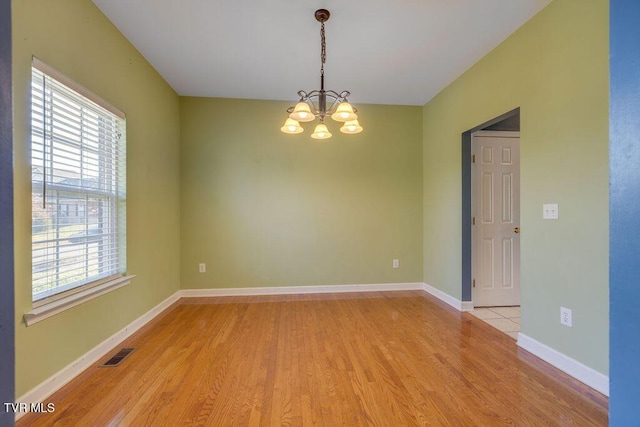 spare room featuring a chandelier, light wood-style flooring, a wealth of natural light, and baseboards