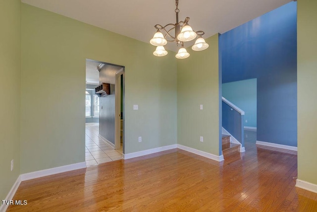 unfurnished room with an inviting chandelier, baseboards, light wood finished floors, and stairs