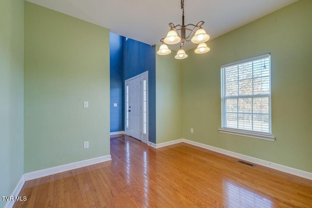 empty room with light wood-type flooring, visible vents, baseboards, and an inviting chandelier