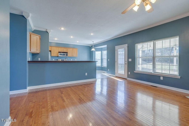 unfurnished living room featuring ceiling fan, visible vents, baseboards, ornamental molding, and light wood finished floors