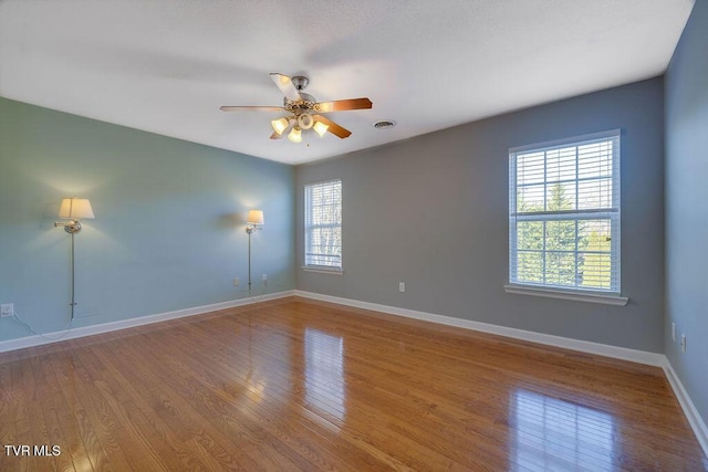 empty room featuring ceiling fan, wood finished floors, visible vents, and baseboards