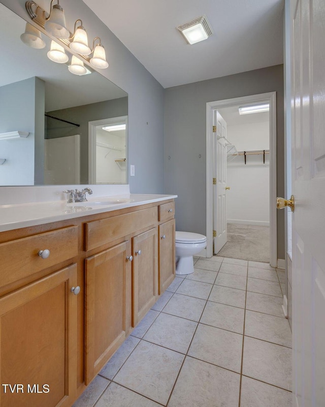 bathroom with a walk in closet, toilet, vanity, baseboards, and tile patterned floors