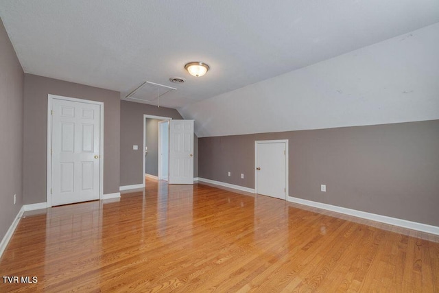 bonus room featuring light wood finished floors, visible vents, attic access, vaulted ceiling, and baseboards