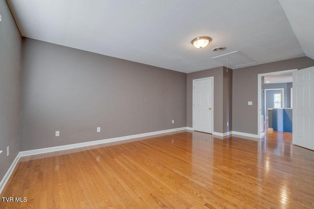 empty room with light wood-type flooring, attic access, visible vents, and baseboards