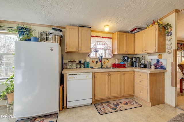 kitchen featuring white appliances, light countertops, a textured ceiling, light brown cabinets, and a sink