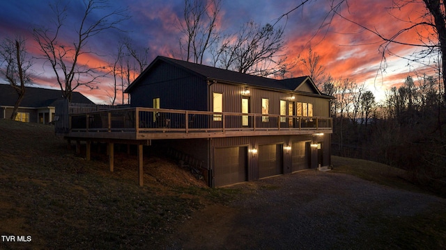 back of property at dusk with driveway, an attached garage, and a wooden deck