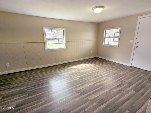 empty room with dark wood-style floors, a wainscoted wall, baseboards, and a healthy amount of sunlight