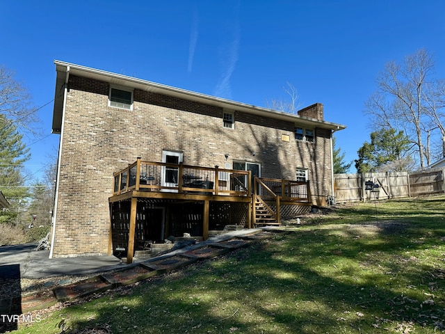 back of house featuring a lawn, a chimney, fence, a deck, and brick siding