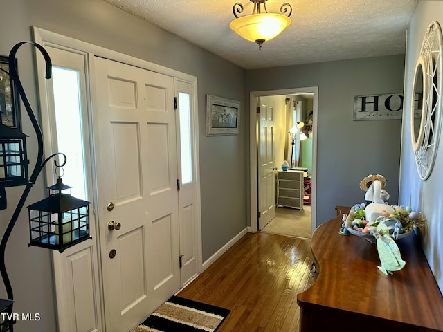 foyer entrance featuring wood-type flooring, a textured ceiling, and baseboards