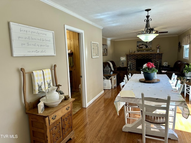 dining area with baseboards, wood finished floors, a textured ceiling, crown molding, and a brick fireplace