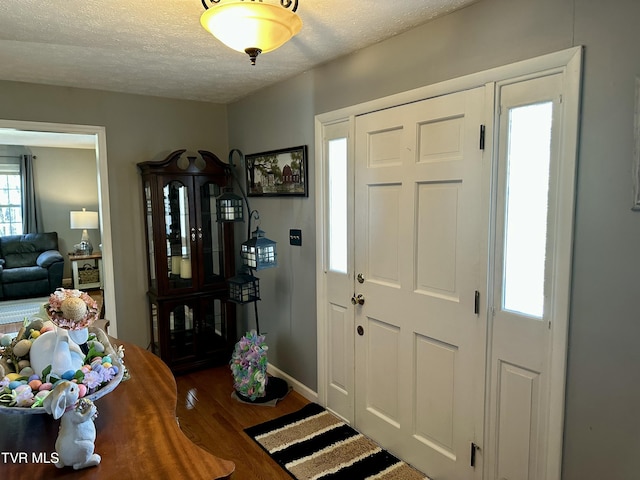 foyer with a textured ceiling, wood finished floors, and baseboards