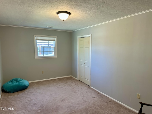 empty room with carpet floors, a textured ceiling, baseboards, and crown molding