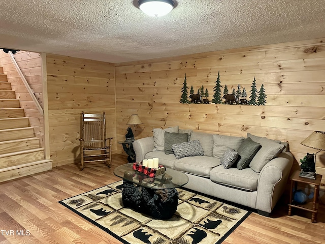 living area with stairs, a textured ceiling, wood finished floors, and wooden walls