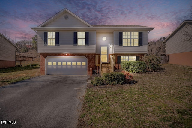 split foyer home featuring an attached garage, a front lawn, aphalt driveway, and brick siding