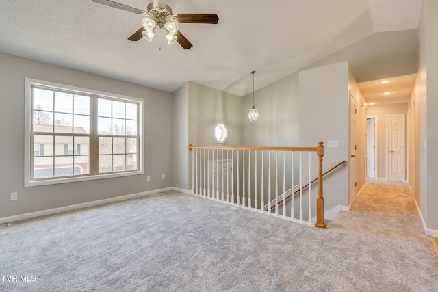 carpeted spare room with a ceiling fan, baseboards, vaulted ceiling, and a textured ceiling