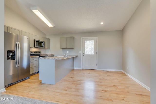 kitchen featuring appliances with stainless steel finishes, a peninsula, vaulted ceiling, gray cabinetry, and light wood-style floors