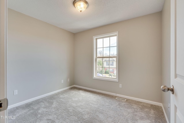 spare room with a textured ceiling, carpet, visible vents, and baseboards