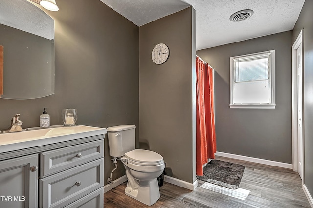 bathroom featuring toilet, wood finished floors, vanity, visible vents, and baseboards