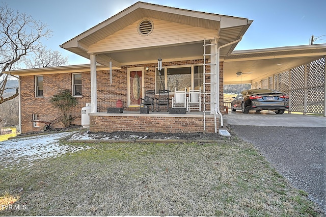 view of front facade featuring driveway, covered porch, a carport, and brick siding